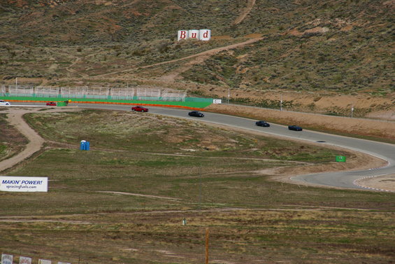 Several cars on a race track with hills and a Budweiser sign in the background
