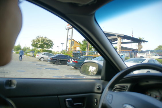 View from inside a car looking out at a parking lot with several cars and a building in the background
