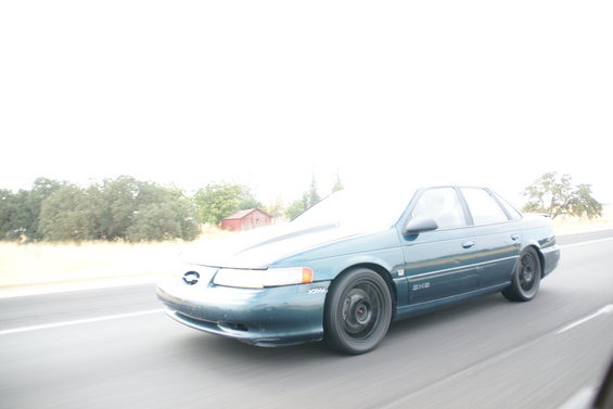 Teal Ford Taurus sedan with black steel wheels driving on a highway
