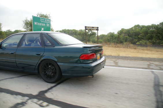 Green 1995 Ford Taurus sedan, rear view, with a spoiler and black wheels