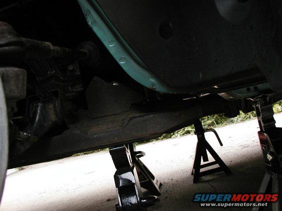 Side view of the removed rear bushing showing the jack stands supporting the car and subframe.