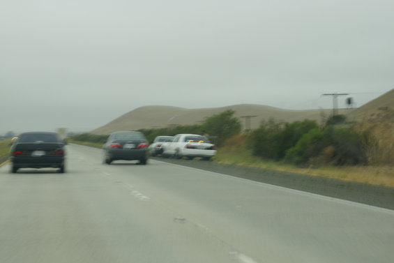 Rear view of three cars on a highway under an overcast sky