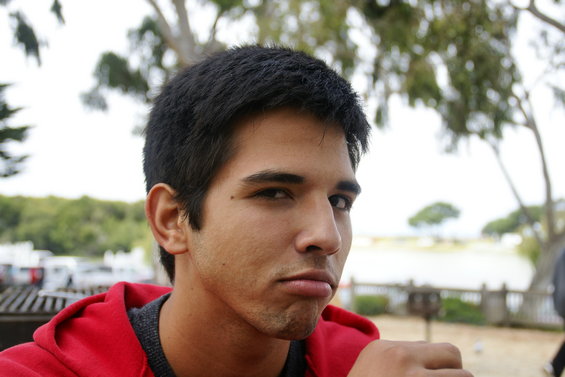 Man with dark hair and a red hoodie makes a pouty face outdoors