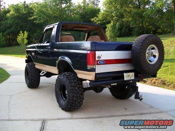 Dark blue and tan Ford Bronco with lifted suspension and large off-road tires, spare tire mounted on rear
