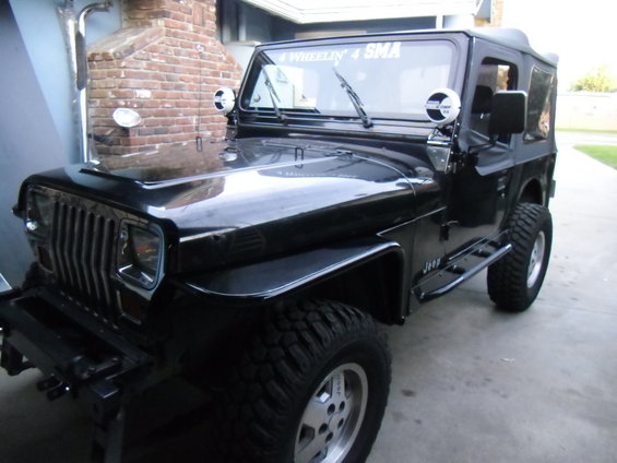 Black Jeep Wrangler parked outside a brick building. It has a soft top and aftermarket side steps