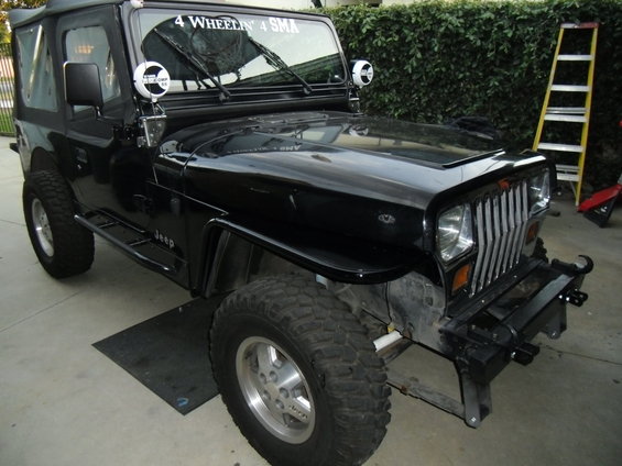 Black Jeep Wrangler, 3/4 front view, aftermarket tube fenders, side steps, custom bumper, ladder in background