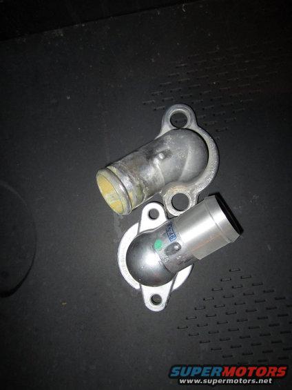 Two metal water neck parts on a dark surface. One is silver with a green dot and blue text, the other is aged metal