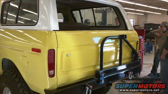 Yellow 1978 Ford Bronco rear quarter view, white hardtop, black spare tire carrier, visible Supermotors logo