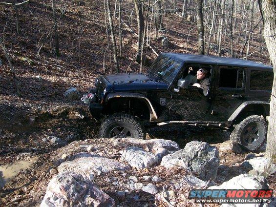 Black 2007 Jeep Wrangler navigating a rocky, muddy off-road trail with a driver visible