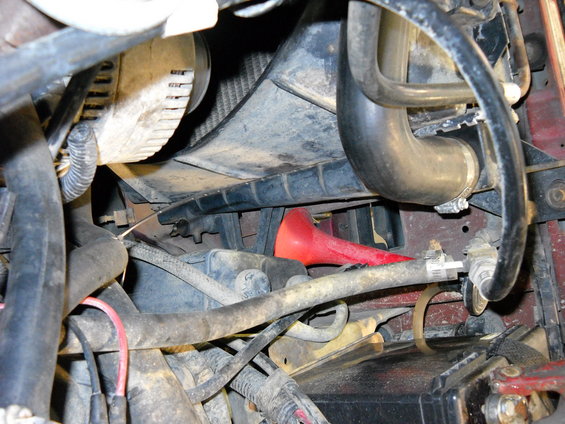 Close-up of engine bay with hoses, fan, and radiator visible. A red funnel is tucked below the radiator