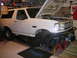 1988 Ford Bronco - This white SUV, likely from the early 1990s, is elevated on jack stands in a garage, indicating it is undergoing maintenance or repair.