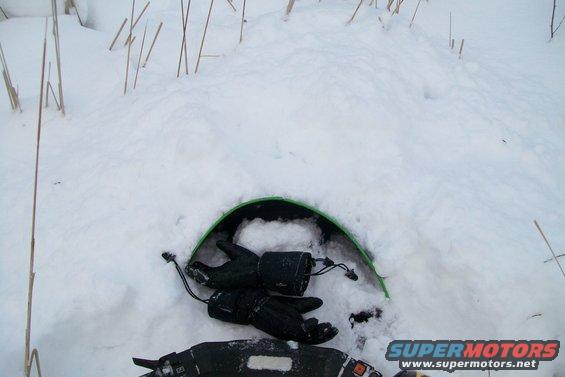 Snowmobile buried in snow with black gloves on handlebars