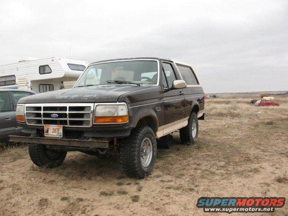 Brown 1992 Ford Bronco parked in a dirt lot with a camper trailer behind it
