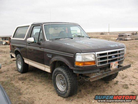 1992 Ford Bronco parked on dirt with a custom bumper and white top