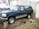 1995 Ford Bronco - A dark green Ford Bronco with tan lower body trim is parked on a grassy area near a mobile home.