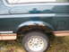 1995 Ford Bronco - The rear wheel well of a dark green SUV shows significant rust and tan lower body trim.