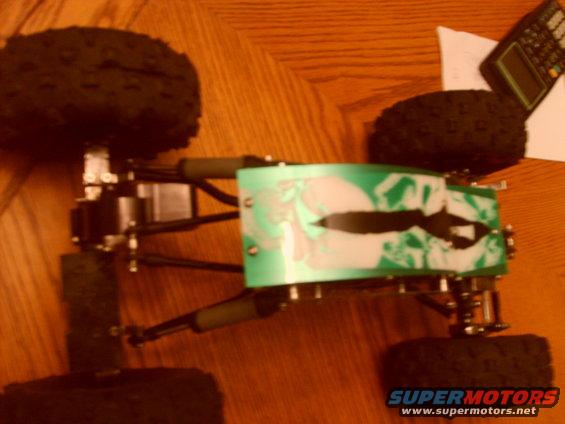 Remote control car chassis with green body, black tires, and suspension components on a wooden surface