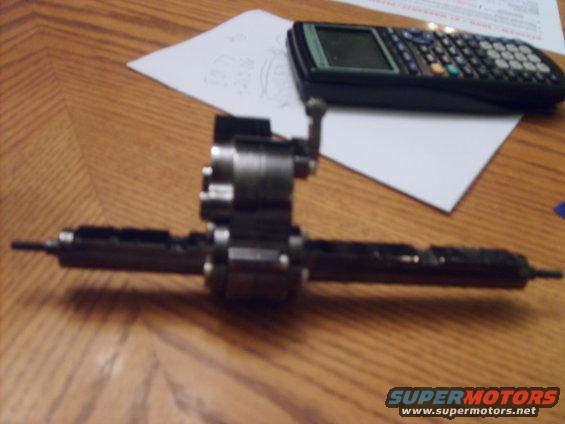 Close-up of a metal automotive differential part on a wooden table next to a calculator and some papers