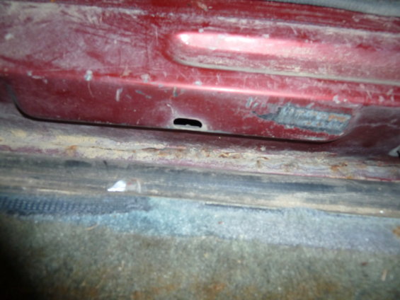 Red interior door sill with visible rust and dirt. A small black hole is present