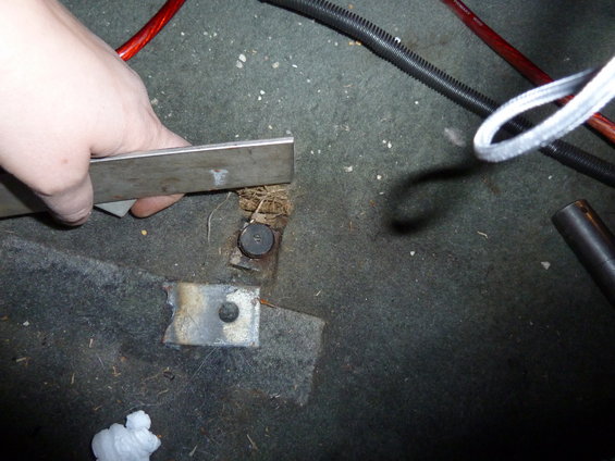 Interior floor with carpet, wiring, and a hand holding a metal bar near a seat bolt