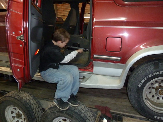Kid sitting in the open door of a red van, reaching inside