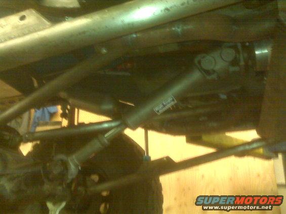 Underside of a vehicle showing driveshaft, u-joints, and suspension parts. Sticker on driveshaft reads 'High Angle Driveline'