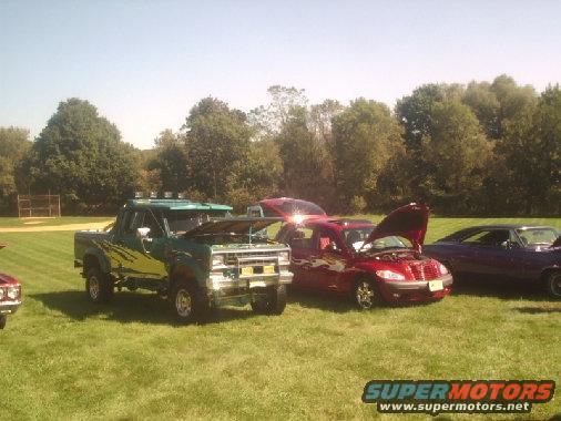 Green pickup truck with yellow graphics and lifted suspension, hood open, parked on grass