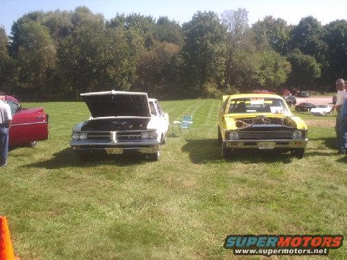 White car with hood up next to yellow car with hood up at outdoor car show