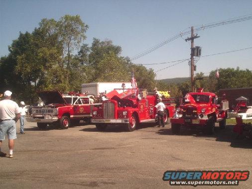 Three red fire trucks parked outdoors, one with hood open