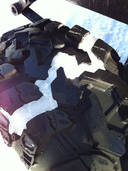 Close-up of a knobby off-road tire with chunks of snow stuck in the tread