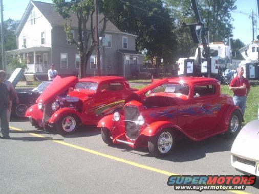 Red hot rod coupe with blue flames, hood up, parked at a car show