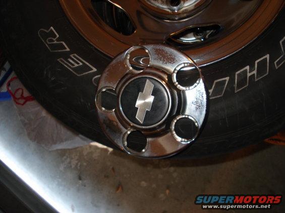 Chrome hubcap with a silver Chevrolet bowtie logo on a black background, resting on a tire