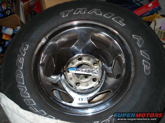 Tire with 'TRAIL FINDER' text on sidewall, mounted on a chrome wheel with a tube of MAAS polish in the center