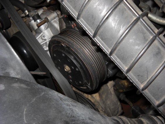 Close-up of engine belt and pulley system, likely an AC compressor clutch