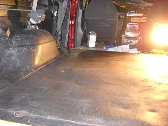 Interior cargo area of a van with black floor, red door frame, and dark grey seats. A bright light is on