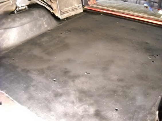 Vehicle interior floor, appears to be a truck bed or cargo area, with black matting and some visible holes