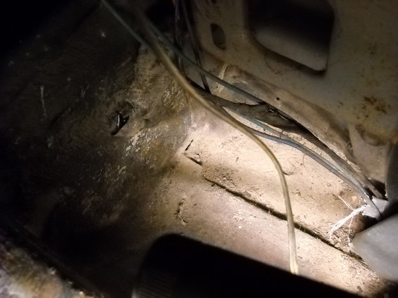 Close-up of a dirty vehicle floor pan with exposed wiring and some debris