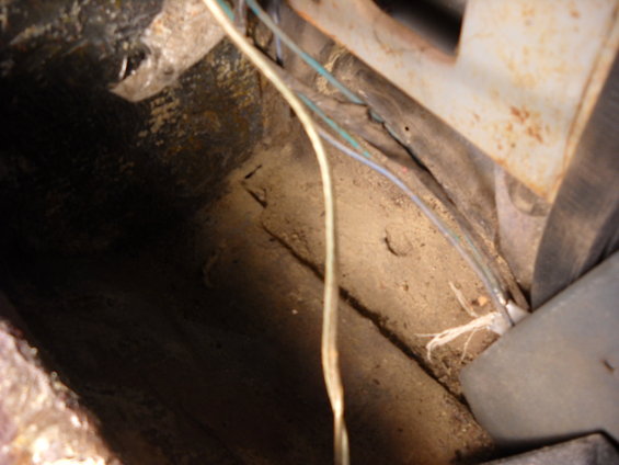 Close-up of a dusty, dirty interior floor area with exposed wiring and metal components