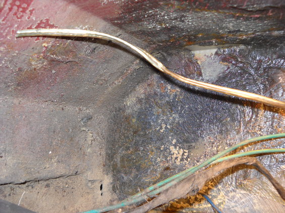 Rusted metal floor pan with exposed wires and conduit