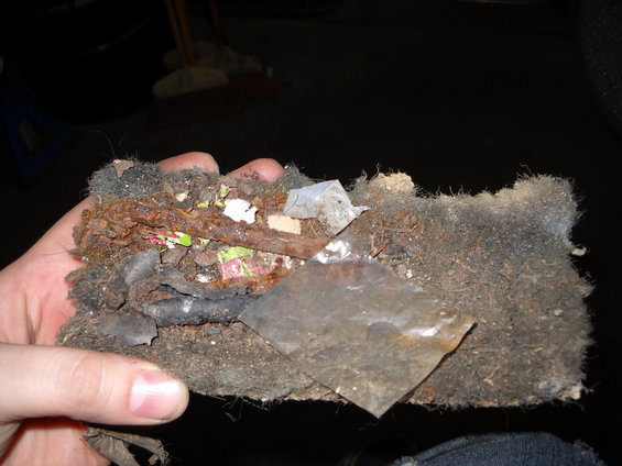 Hand holding a clump of dirt, rust, and debris, possibly from a car's interior