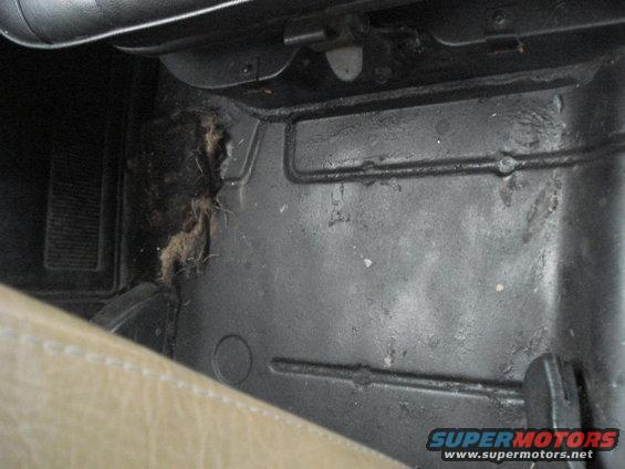 Interior floor of a vehicle showing dirt and debris accumulation near the seat and dashboard