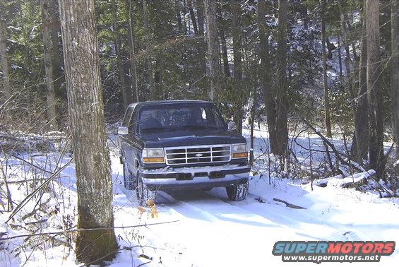 dark 1995 Ford Bronco driving on a snowy path through trees