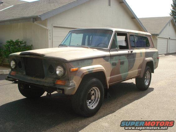 Camouflaged Jeep Cherokee with aftermarket wheels parked in front of a garage