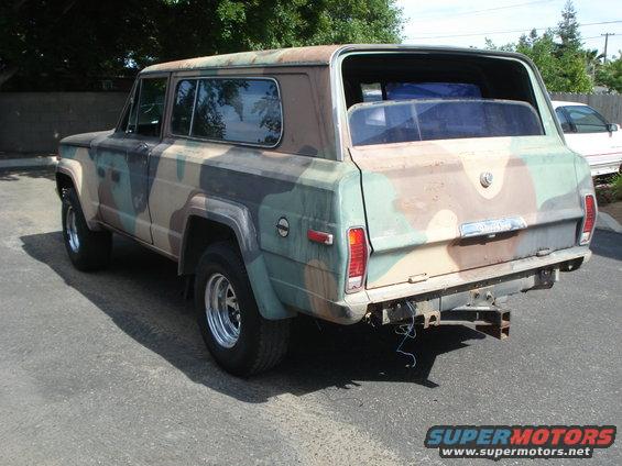 Camouflaged Jeep Wagoneer, rear quarter view. Has a trailer hitch. Another car is visible in the background