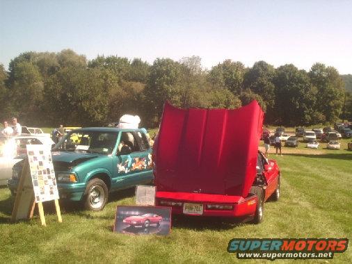 red sports car with hood up, green SUV with cartoon decals, parked on grass at car show
