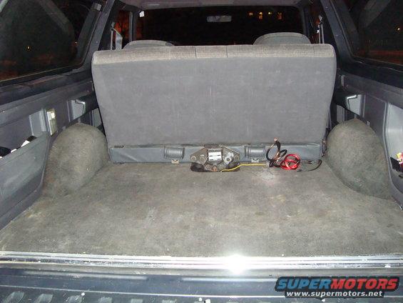 Back cargo area of an SUV with carpeted floor and wheel wells, showing a folded rear seat and some wiring