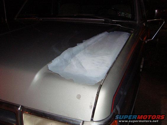 Silver Ford Bronco hood with peeling clear coat and a white cloth covering part of the damage