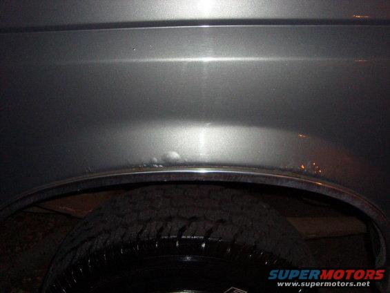 Close-up of a dent and rust on the rear wheel well of a gray vehicle