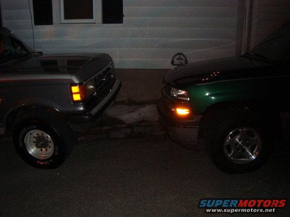 Gray truck on left, green truck on right, parked close together in front of a house