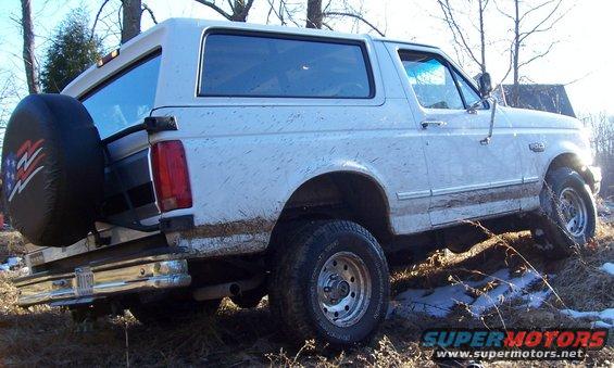 White Ford Bronco with a spare tire on the back, covered in mud, parked on uneven terrain